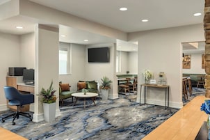 A modern hotel lobby with a marble floor, seating areas, a reception desk, and a TV mounted on the wall.