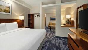 A hotel room with a large bed, a desk with a television, a wardrobe, a seating area with a sofa, and a painting on the wall.