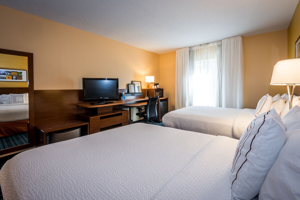 A hotel room with two beds, a desk with a computer, a television, and a window with curtains.