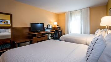 A hotel room with two beds, a desk with a computer, a television, and a window with curtains.