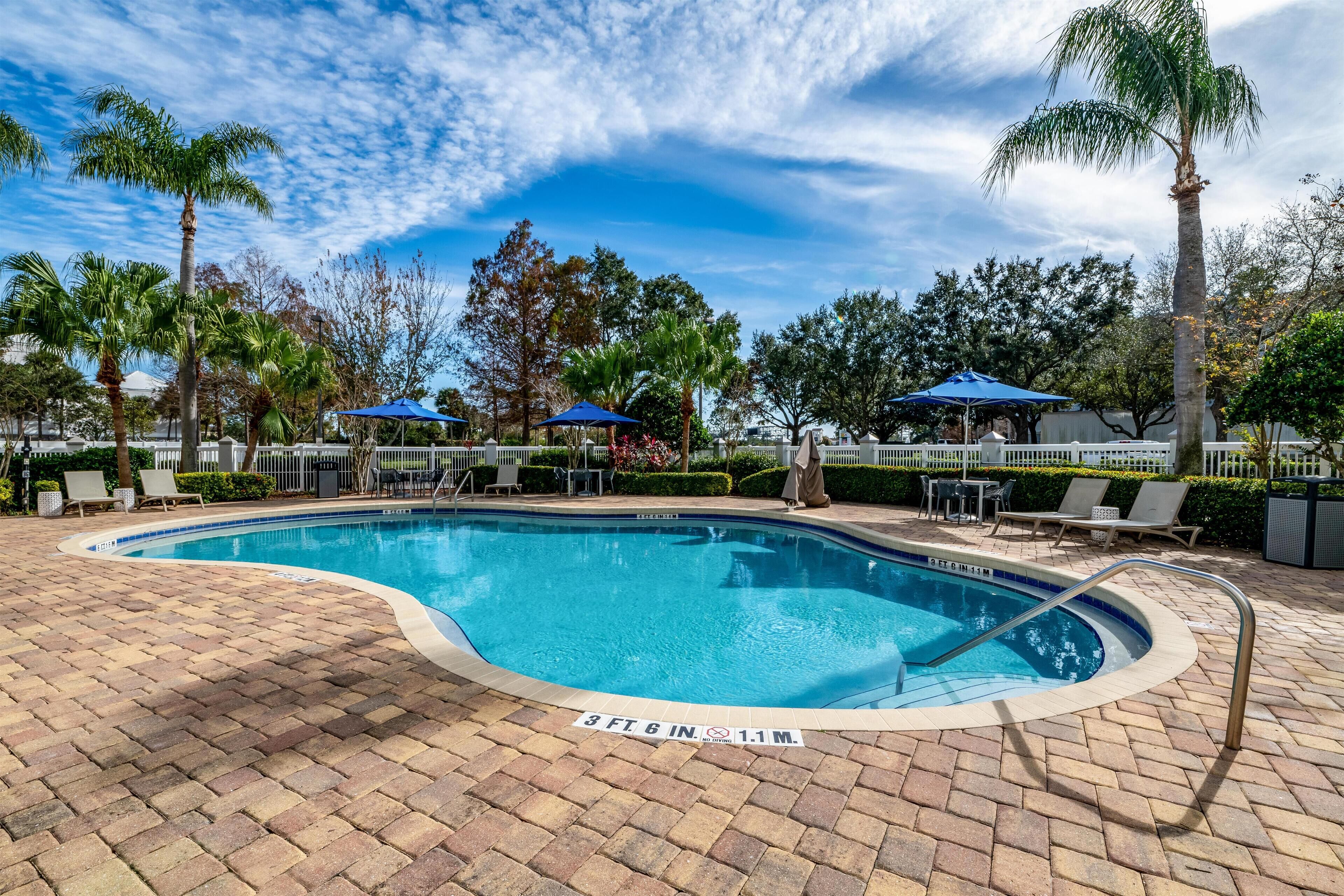 Ein Swimmingpool mit Pflasterterrasse, Palmen und Liegestühlen.