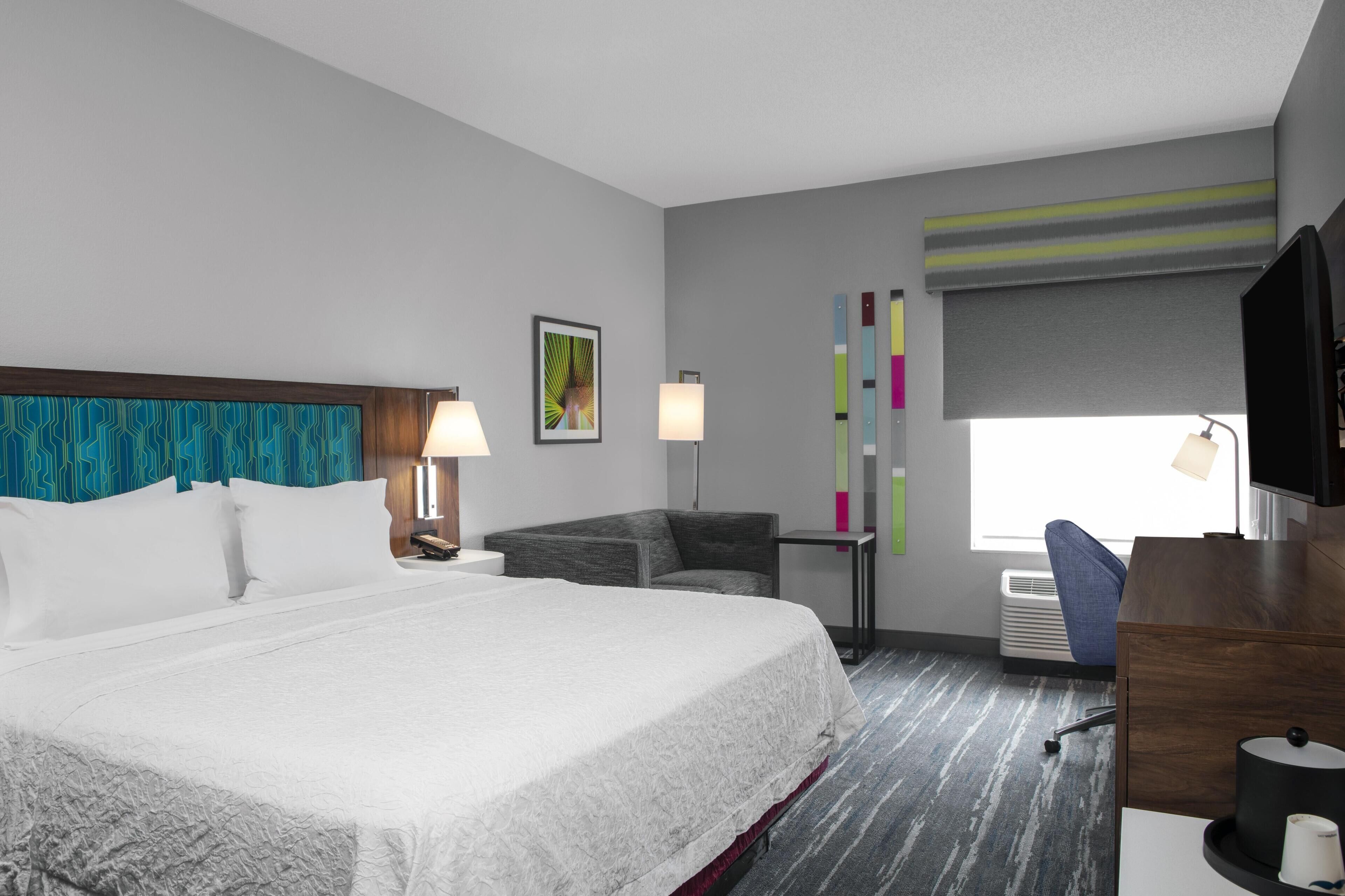 Une chambre d’hôtel avec un grand lit, un bureau, une chaise, une télévision et une fenêtre donnant sur un beau paysage.