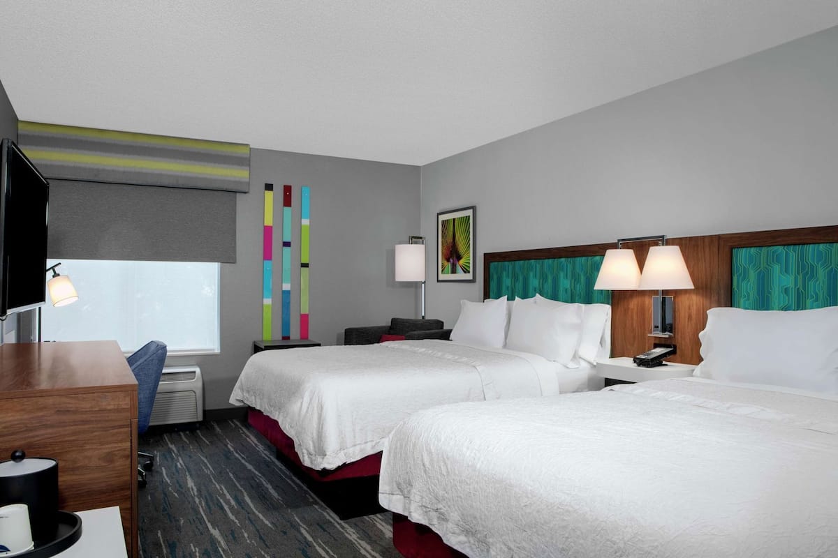 Habitación de hotel con dos camas, un escritorio, un televisor y una ventana.
