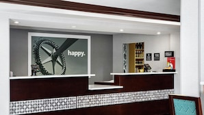 Et hotellets receptionområde med et moderne design, inklusive en reception, et stort spejl og en dekorativ væg med et cirkulært mønster.