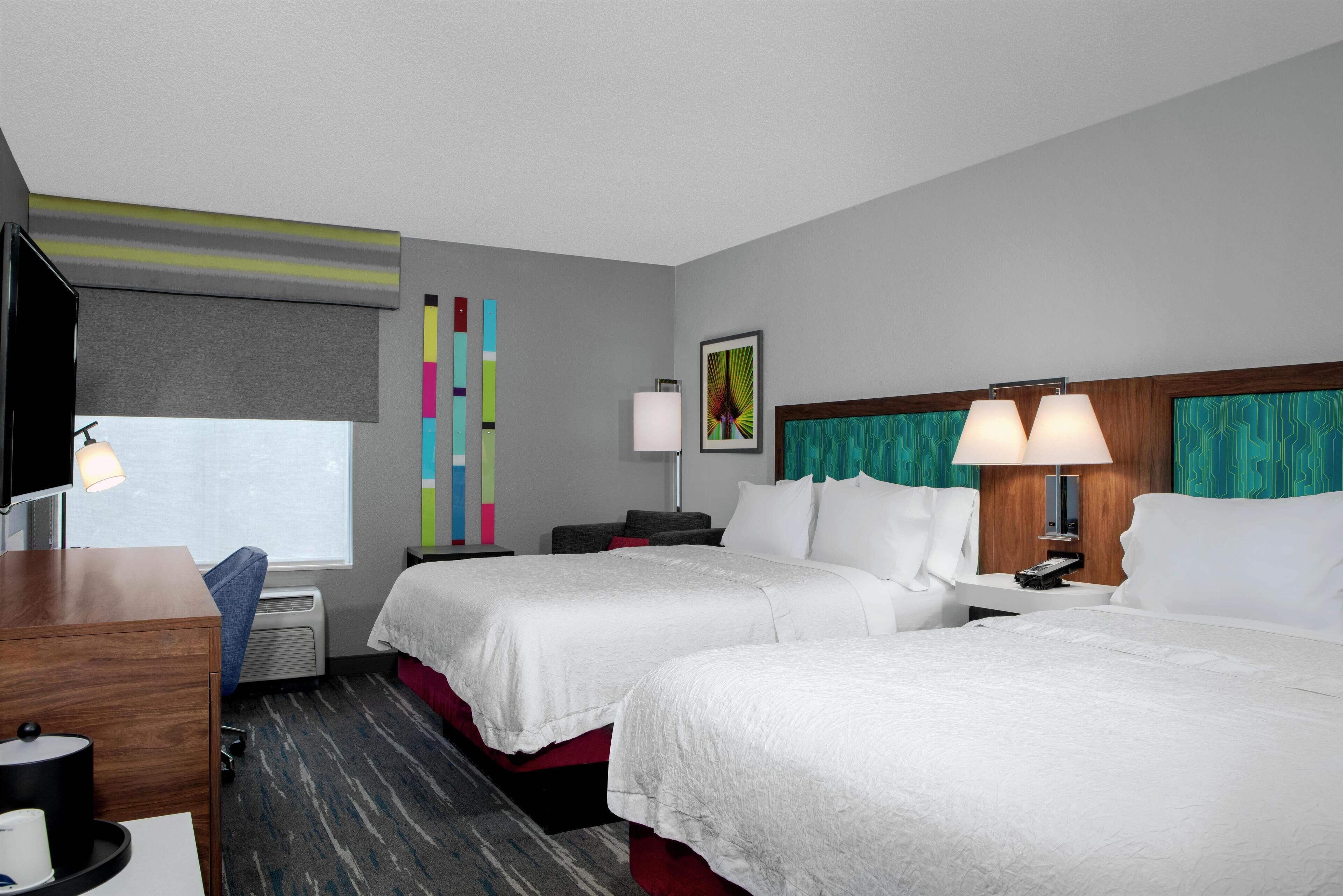 Habitación de hotel con dos camas, un escritorio, un televisor y ventana con vistas.