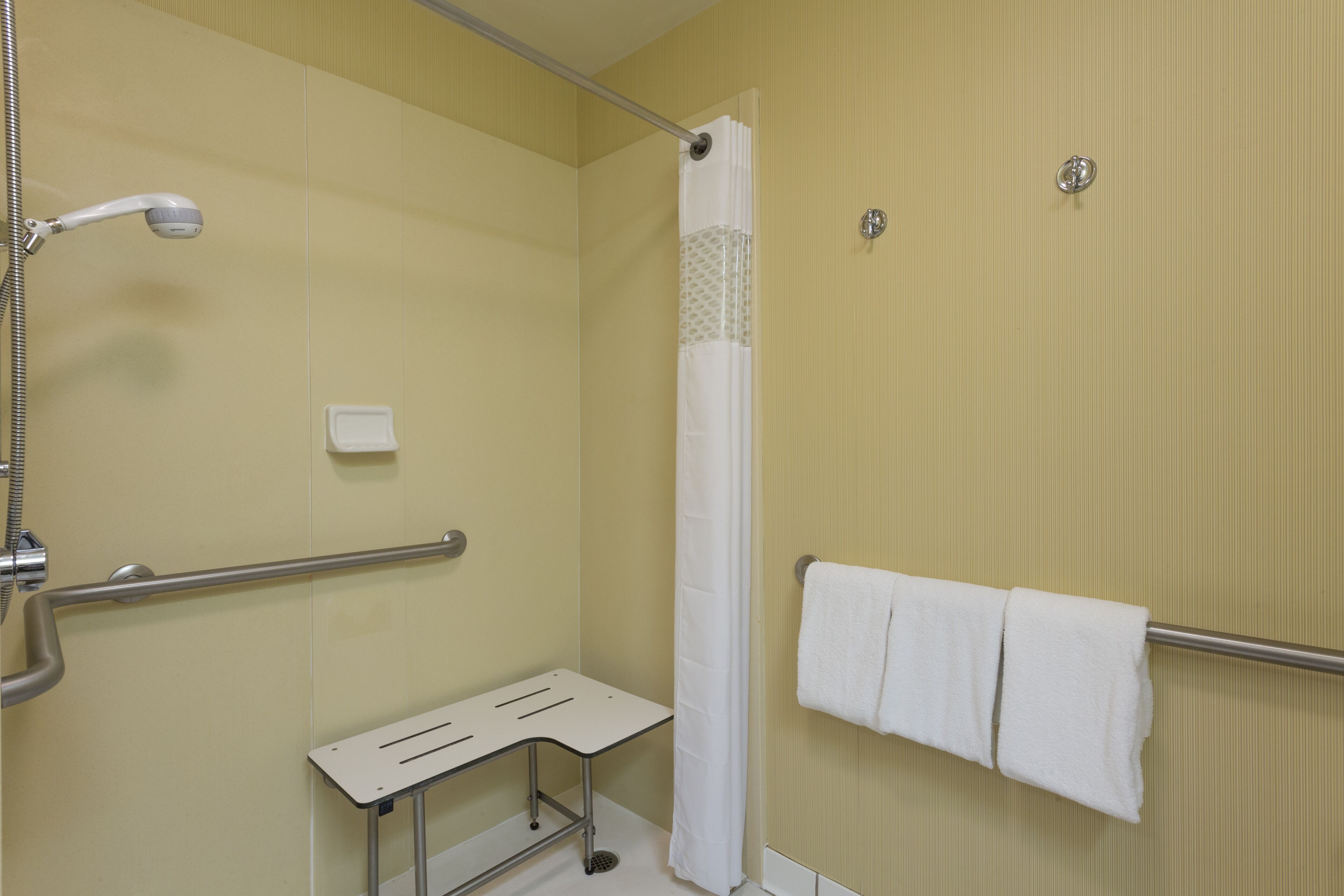 Une salle de bain équipée d’une douche, de barres d’appui, d’un banc, d’un porte-serviettes et d’un support à papier toilette.