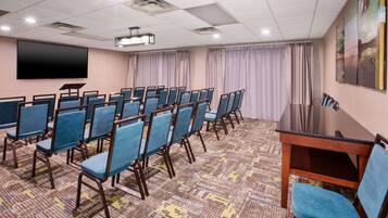 Un salón de conferencias con filas de sillas azules, una pantalla de proyector y un cuadro grande en la pared.