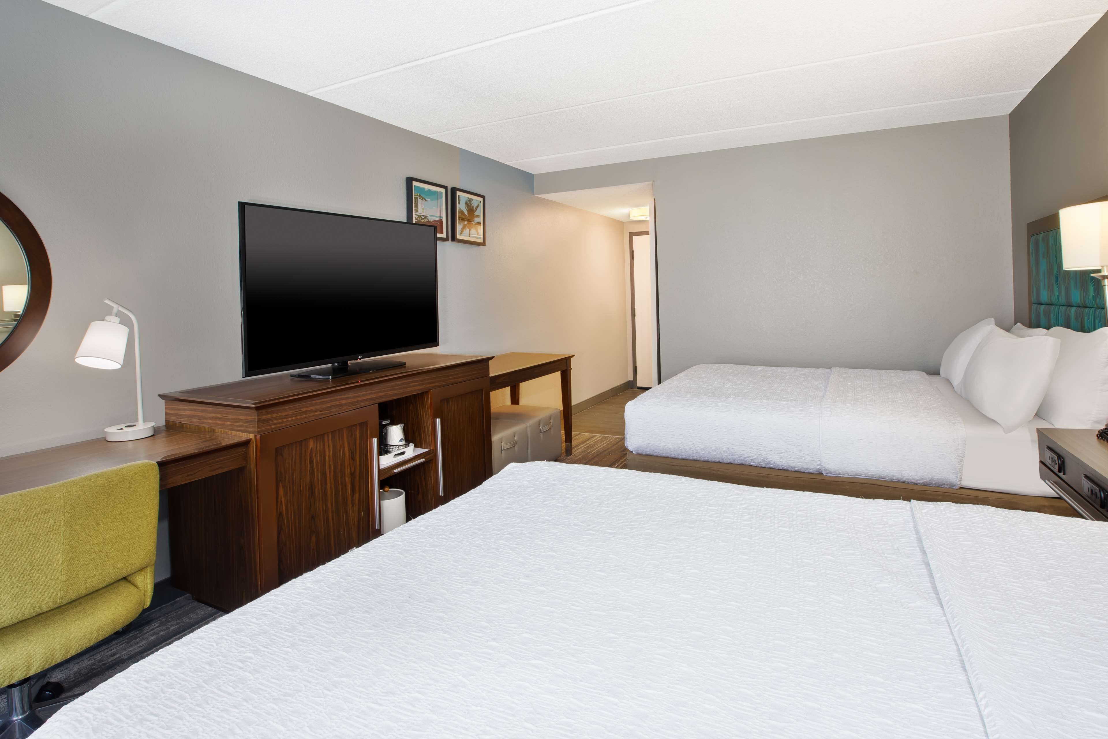 A hotel room with two beds, a TV, a desk with a lamp, and a mirror.
