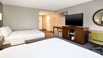 A hotel room with a large bed, a desk with a television, a chair, and a small table.