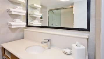 A modern bathroom with a large mirror, white sink, and towel racks.