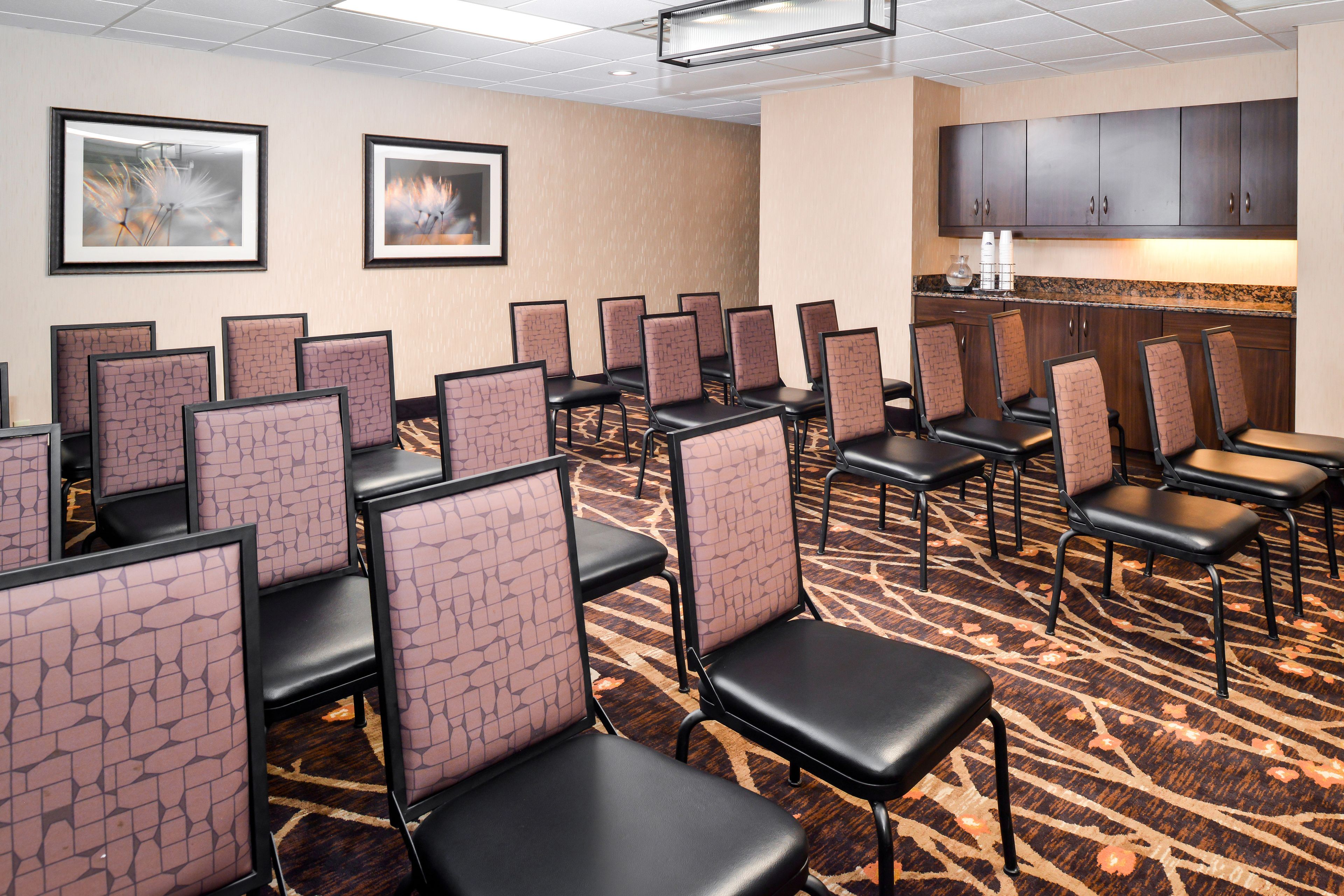 A hotel room with rows of individual seating areas, a kitchenette, and framed artwork on the walls.