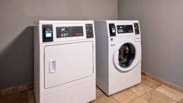 Two front-loading washing machines in a laundry room with tiled flooring and a plain wall.