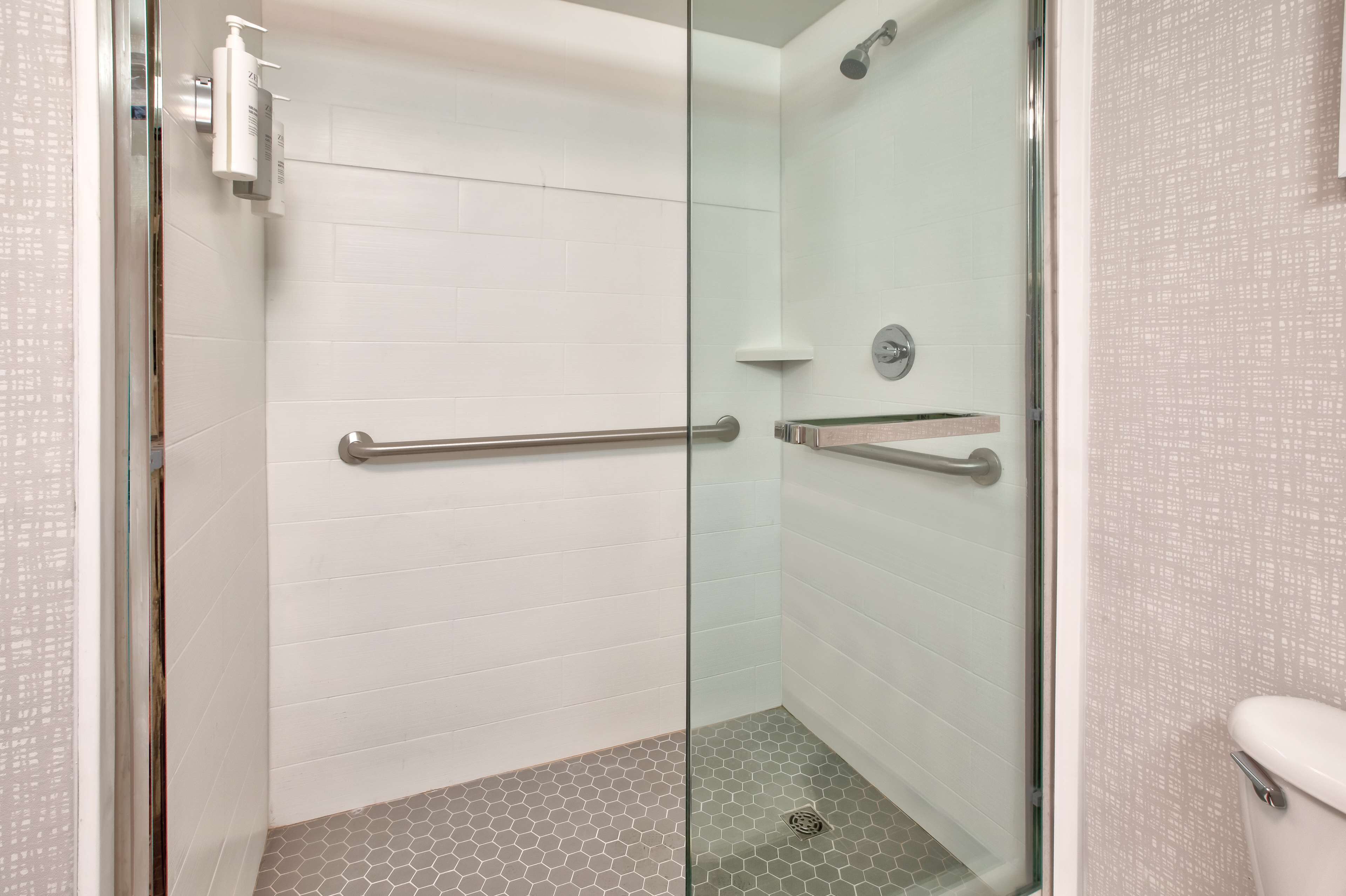 A modern bathroom with a glass shower enclosure, white tiled walls, and a hexagonal floor pattern.