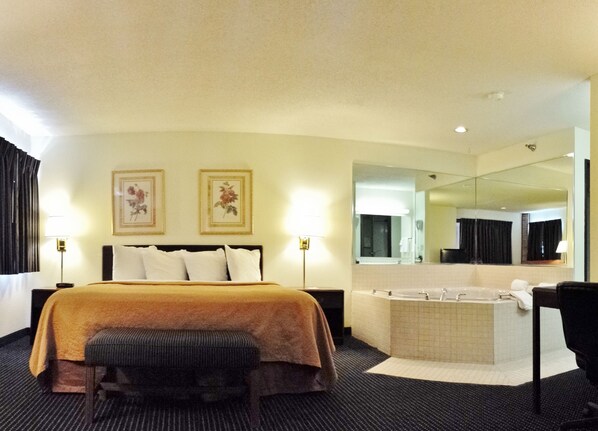 A hotel room with a bed, a large mirror, a bathtub, and two wall-mounted lamps. - Quality Inn Dundee (Dundee)