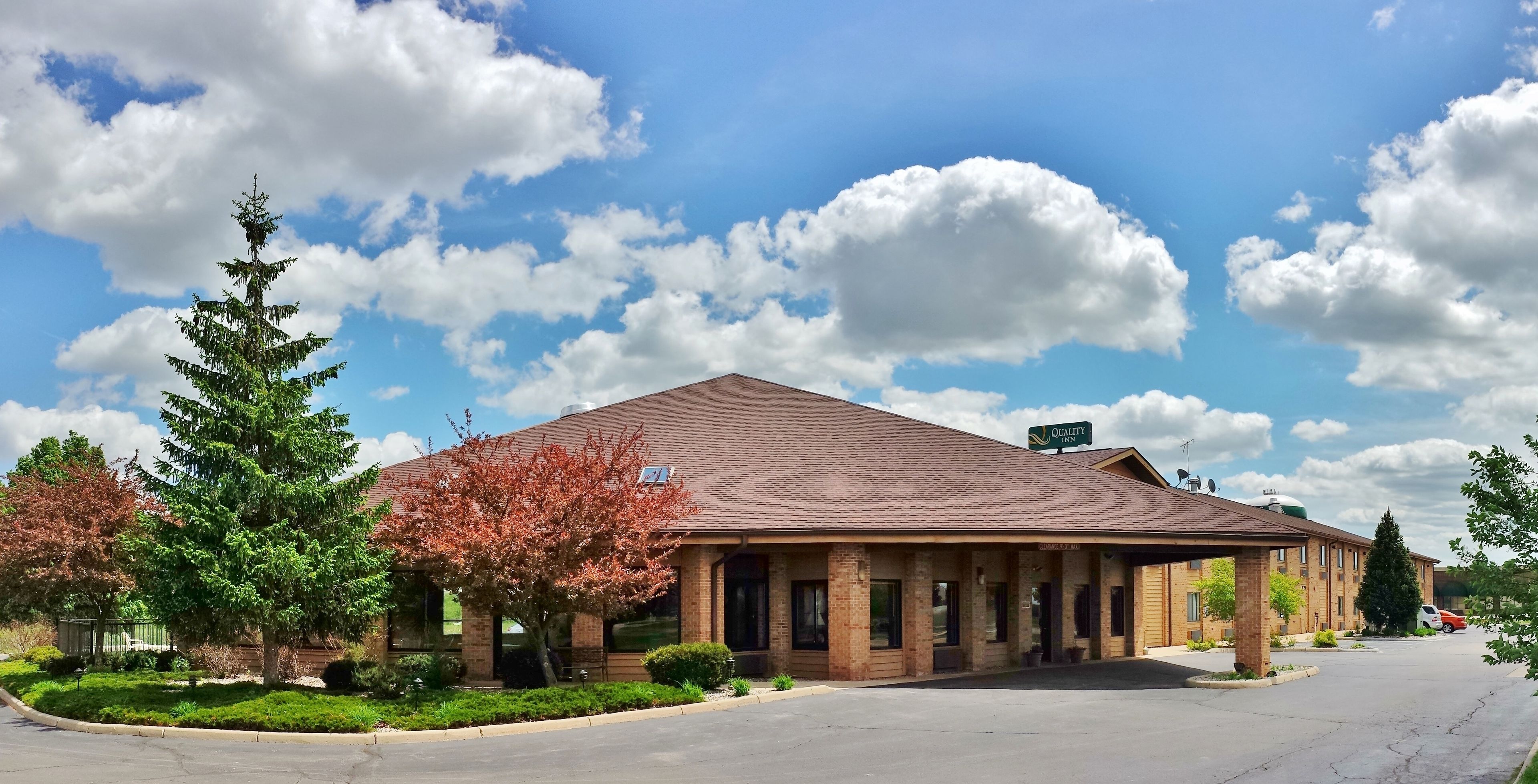 A building with a brick facade, a sign reading "Quality Inn," and a parking lot with a few cars.