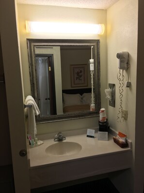 Un baño de hotel con un espejo grande, un lavamanos, un secador de pelo y un perchero para toallas.