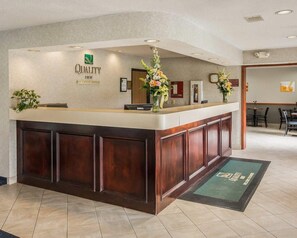 Una zona reception di un hotel con una scrivania in legno, un computer Dell e un'asse floreale.