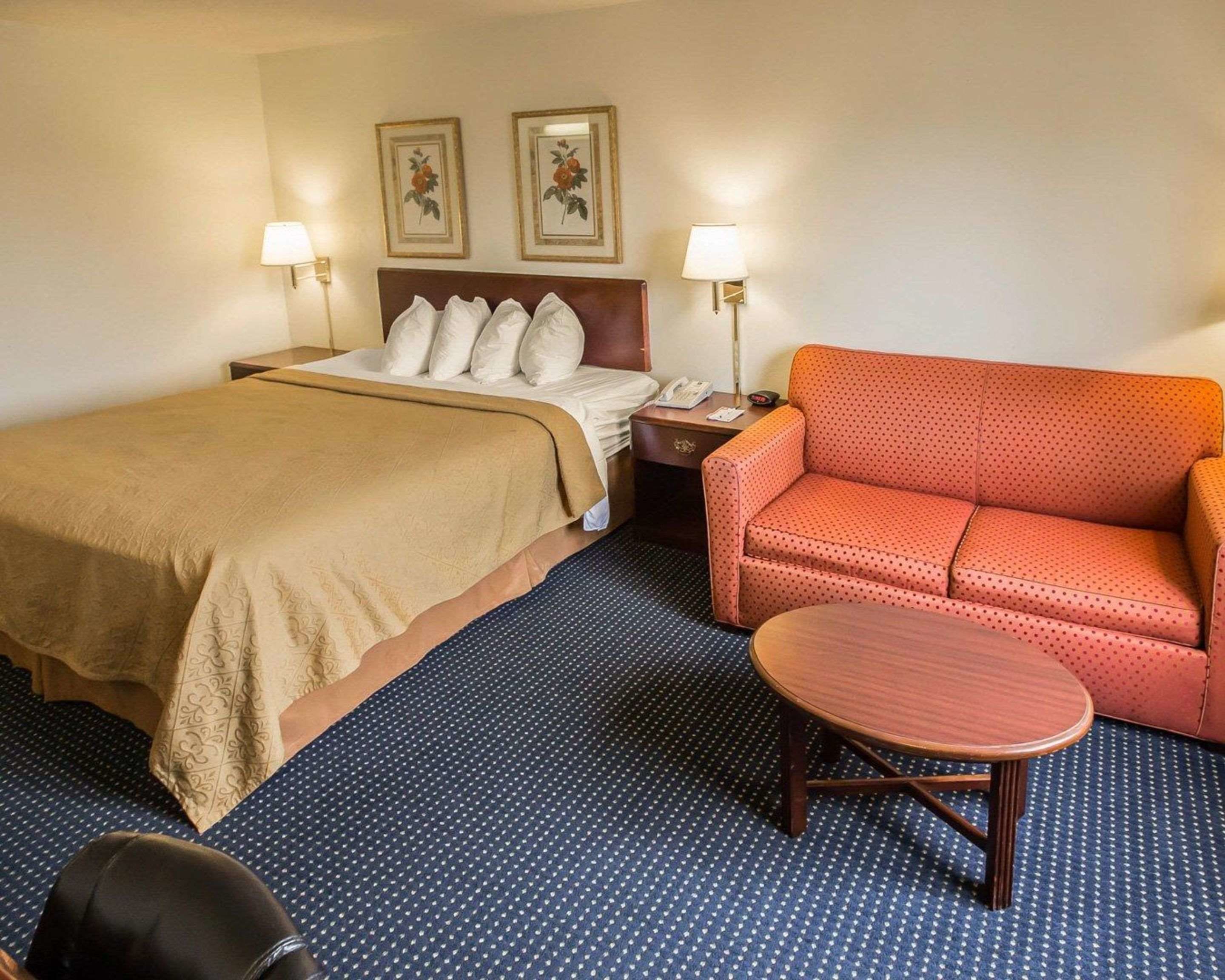 Une chambre d’hôtel comprenant un lit, un canapé, une table et deux lampes fixées au mur.