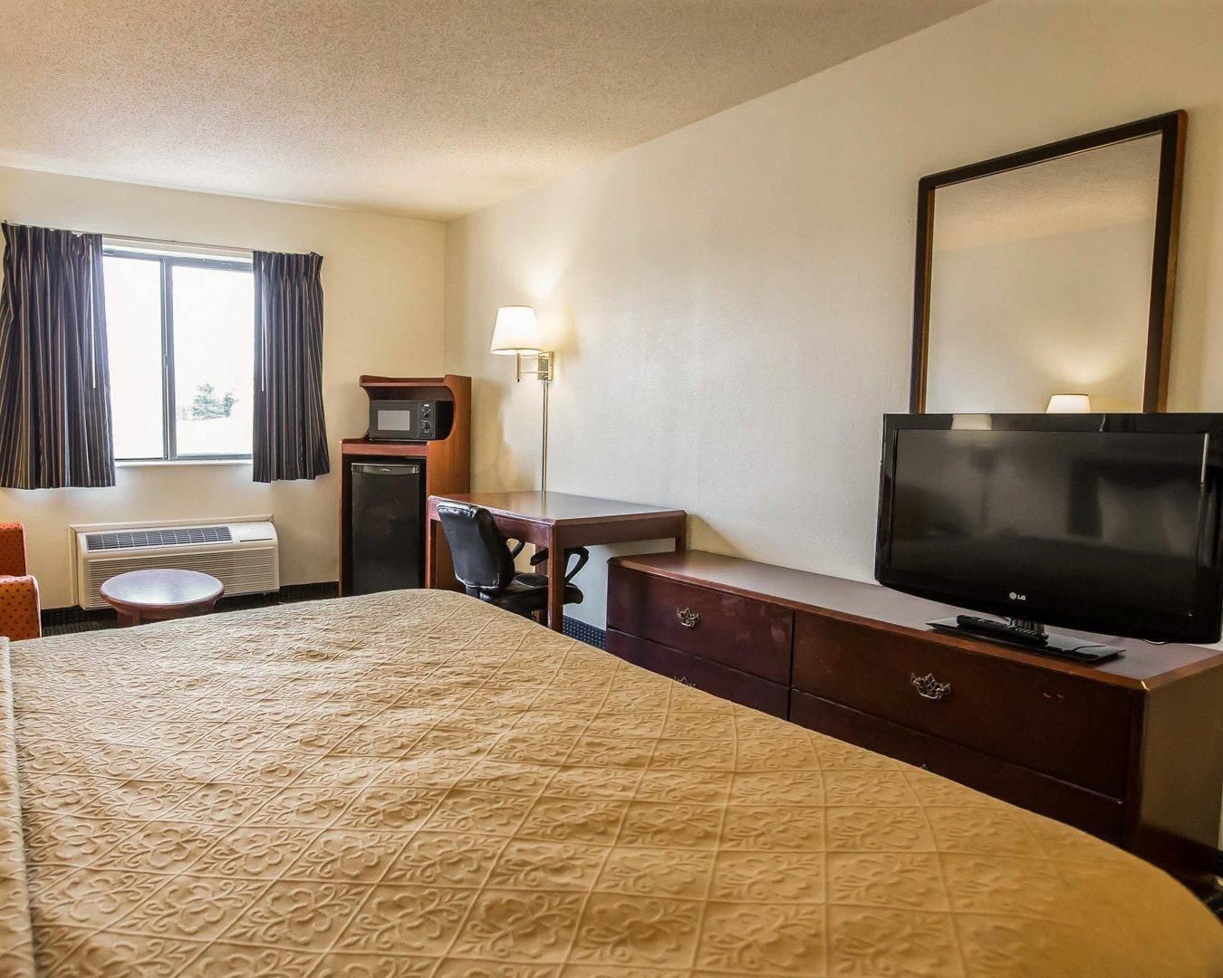 Habitación de hotel con cama, escritorio con lámpara, televisión y ventana con cortinas.