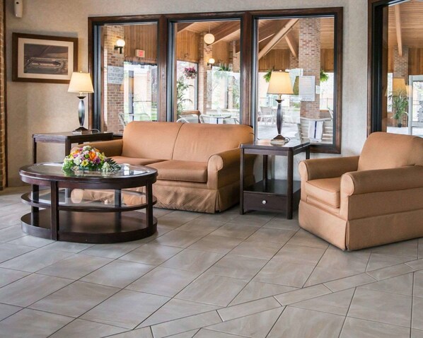 A modern living room with beige sofas, a round coffee table with a floral centerpiece, and a glass-top side table. - Quality Inn Dundee (Dundee)