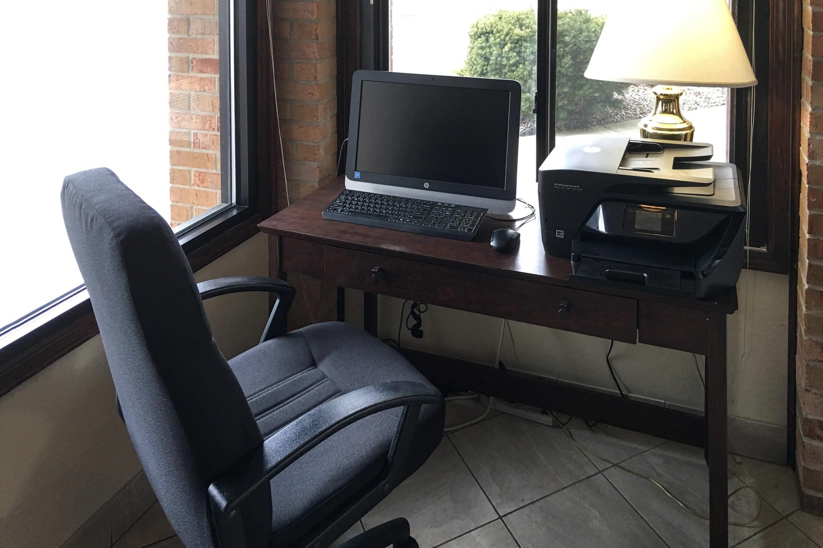 A workspace with a desktop computer, a printer, a lamp, and a chair.