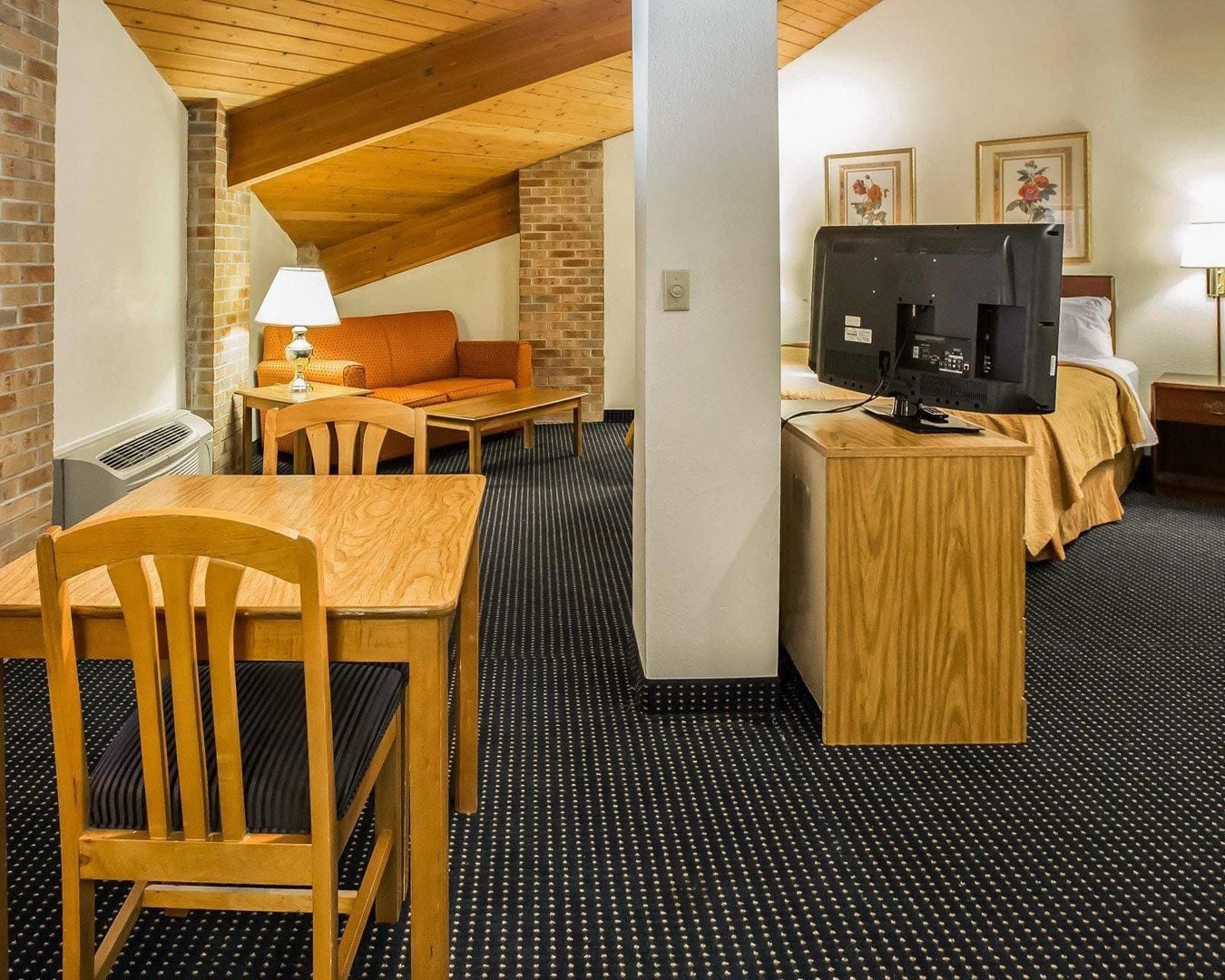 Een hotelkamer met een houten tafel, een bank, een televisie op een houten dressoir en een kamerbreed tapijt met een patroon.