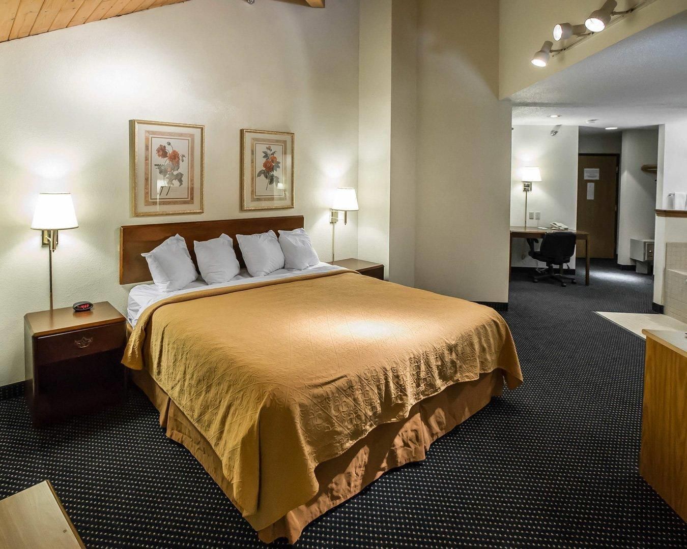 A hotel room with a large bed, two bedside lamps, a desk, and a chair.