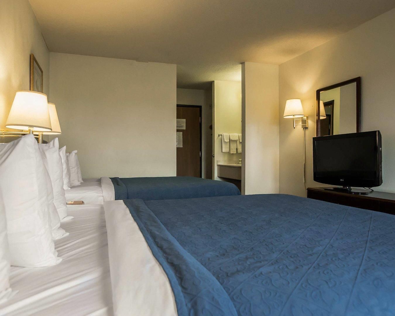 A hotel room with two beds, a television, and a bathroom visible through an open door.