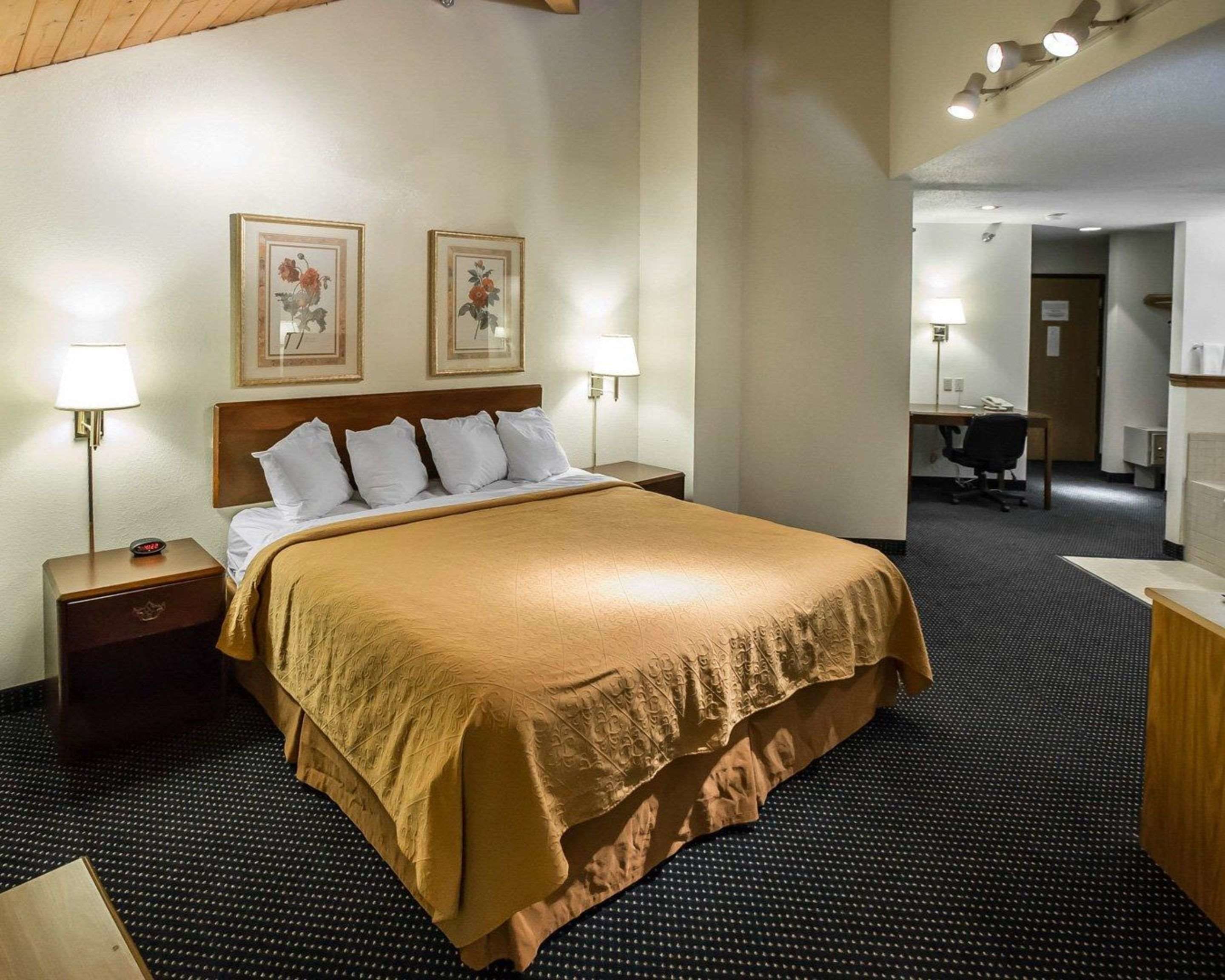 A hotel room with a large bed, two bedside lamps, a desk, and a chair.