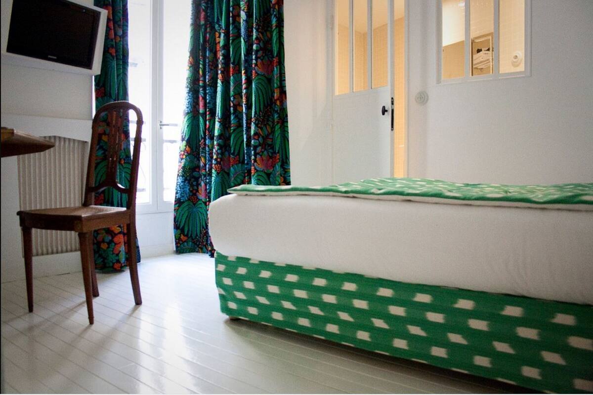 A bedroom with a bed, a chair, a television, and a door with a window.