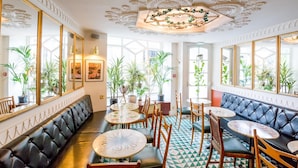 A restaurant with a black leather booth seating, round tables, and potted plants.