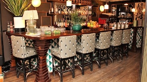 A bar area with a wooden bar counter, multiple bar stools, and a variety of bottles and glasses on shelves.