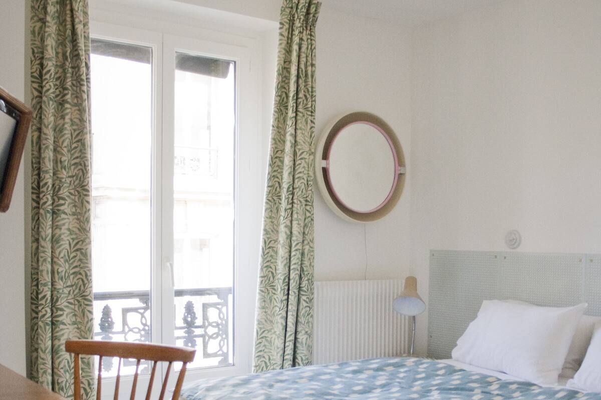 A bedroom with a bed, a chair, a table, and a window with curtains.