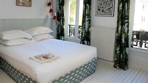 A bedroom with a bed, white bedding, a window with curtains, and two framed artworks on the wall.