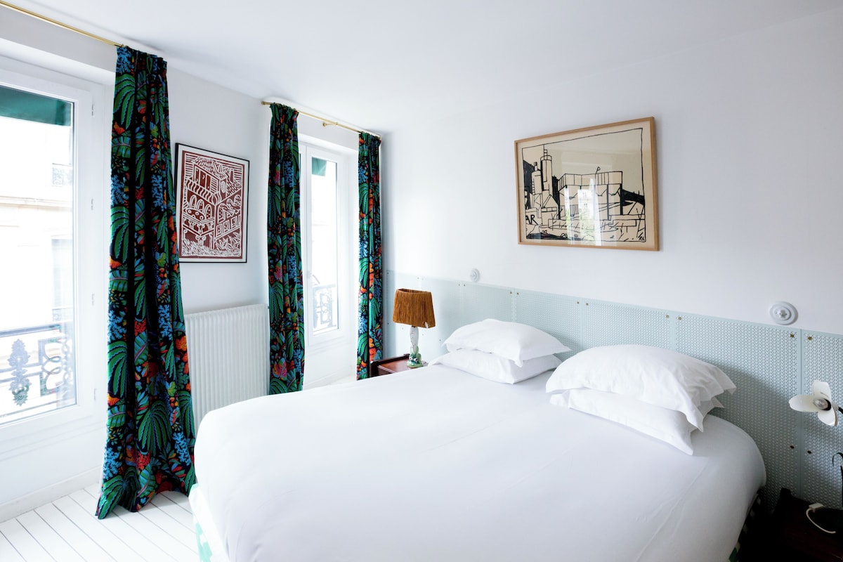 A hotel room with a large bed, a nightstand, a lamp, a window with curtains, and a framed picture on the wall.