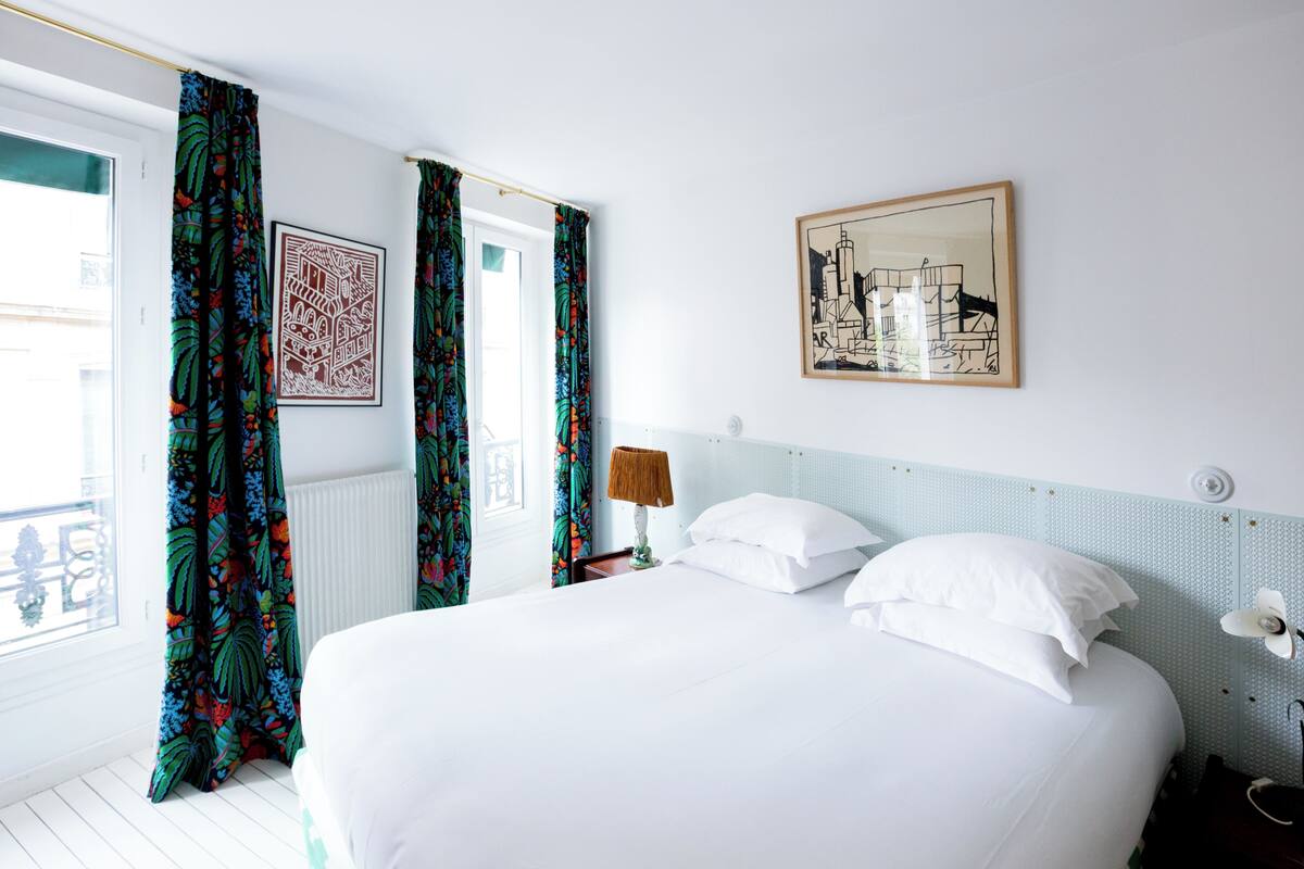 A hotel room with a bed, curtains, a lamp, a framed picture, and a window.