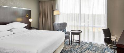 Hotelkamer met een groot bed, een bureau, een stoel, een lamp en uitzicht op de stad.