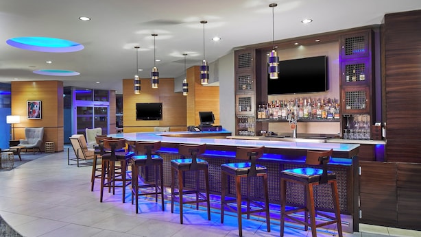 Zona de bar moderna con mostrador, varios taburetes y un televisor montado en la pared.