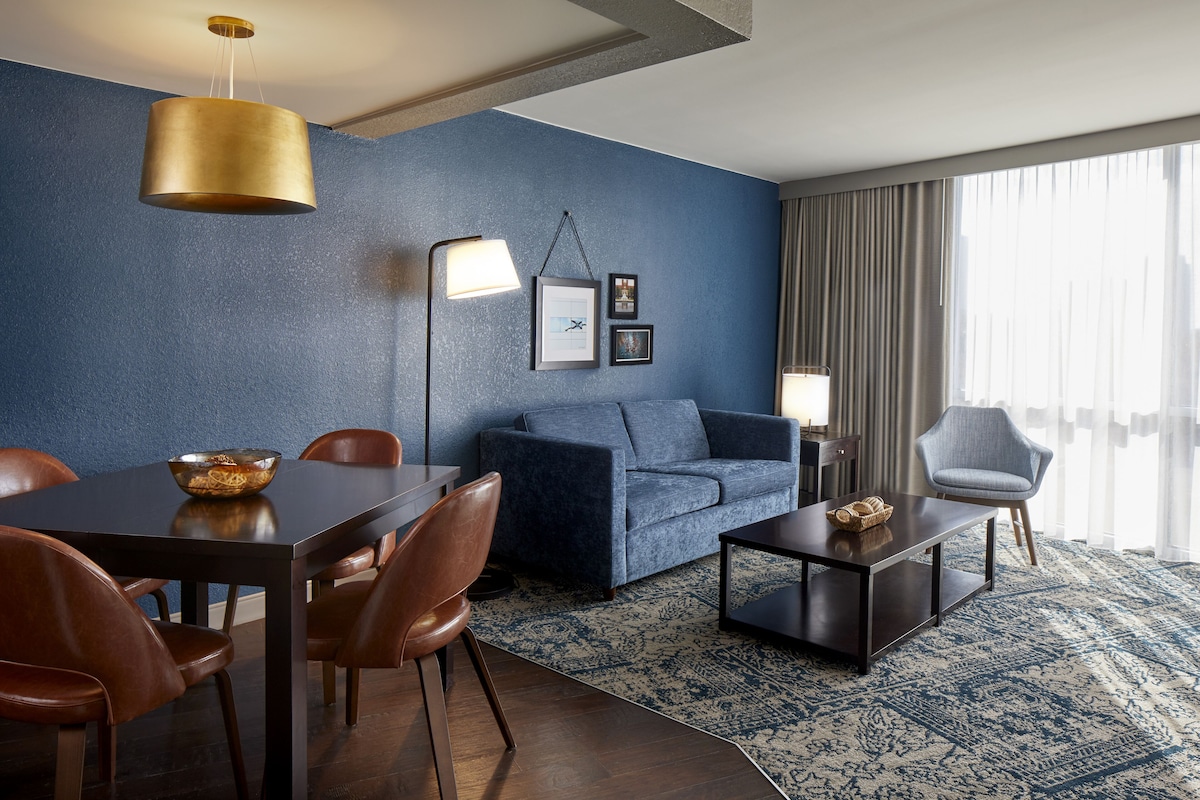 Un salon moderne avec un mur d’accent bleu, un coin repas avec des chaises en bois, un canapé et une table basse.