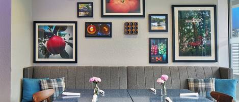 A dining area with a booth seating arrangement, framed artwork on the wall, and a table set with a vase of flowers.