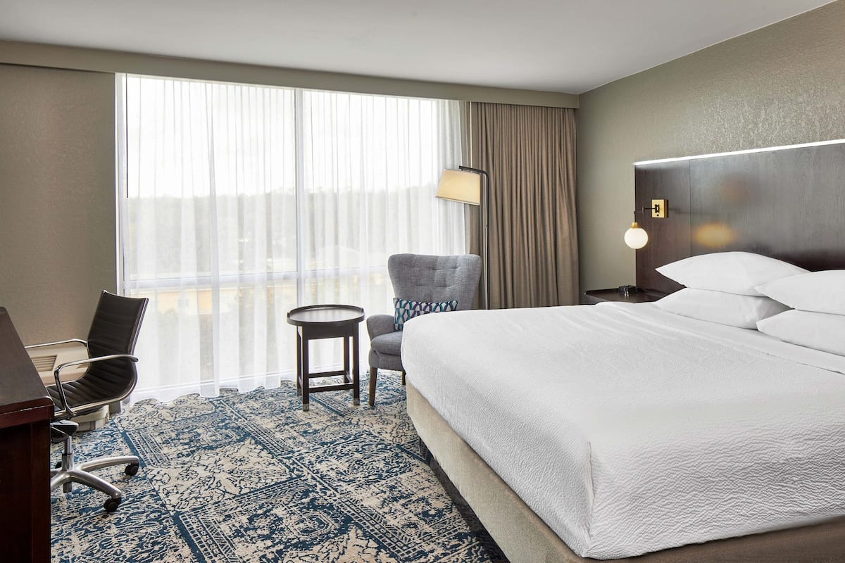 Habitación de hotel con una cama grande, un escritorio con silla, una mesita redonda y una lámpara.