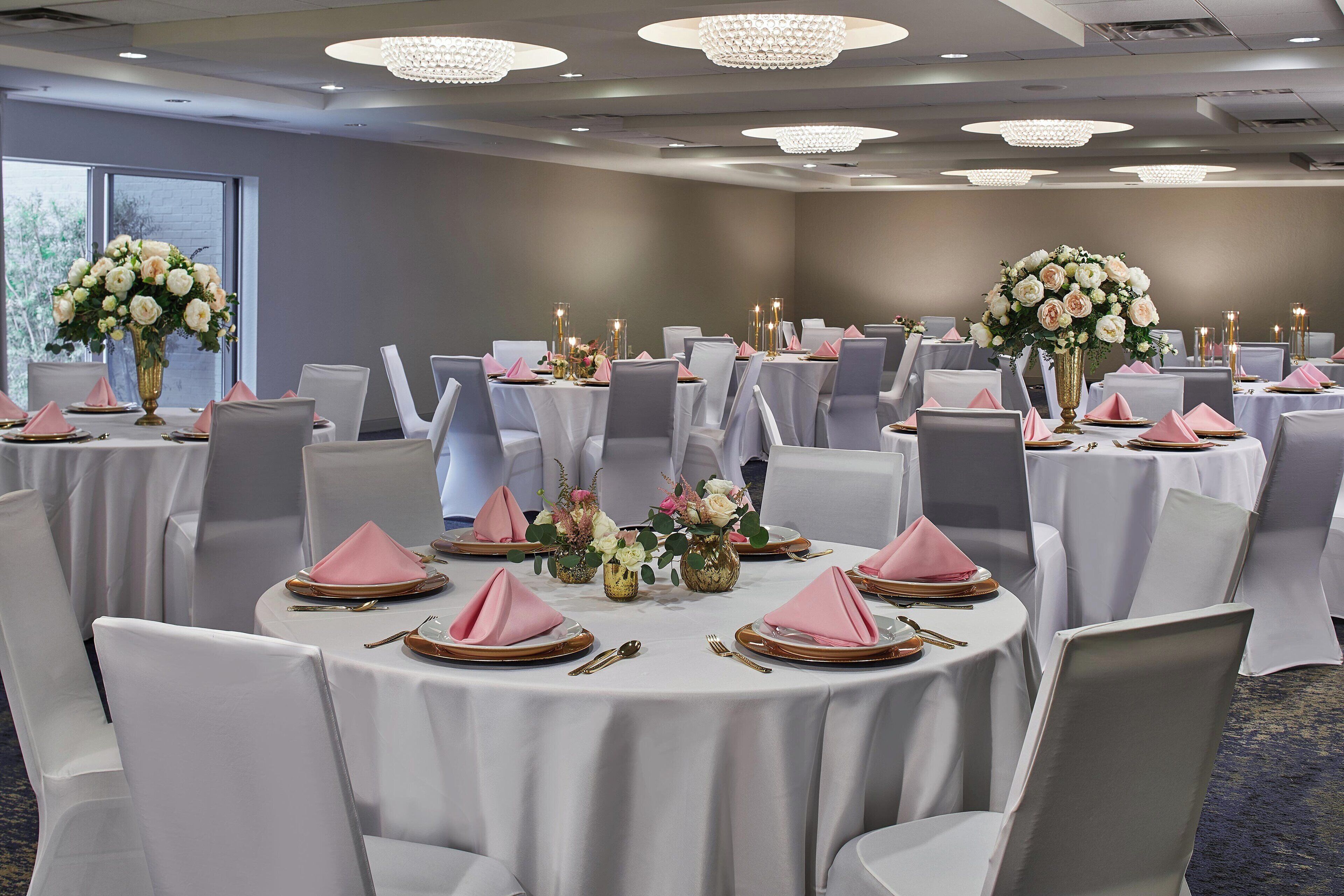 A banquet hall with round tables, white tablecloths, and pink napkins.