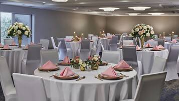 A banquet hall with round tables, white tablecloths, and pink napkins.