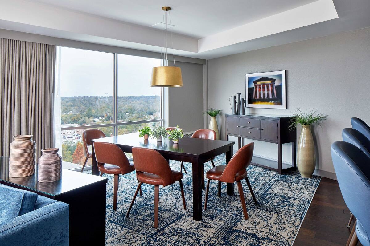 Un moderno comedor con un amplio ventanal, una mesa de comedor con sillas y vistas al paisaje urbano.