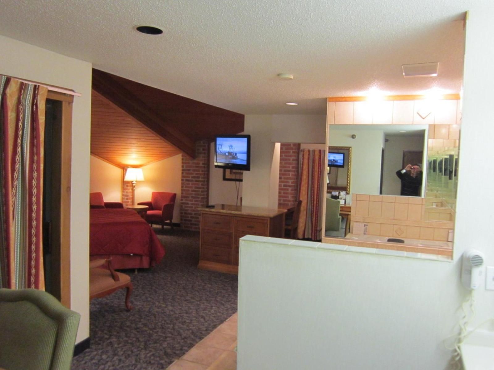 Una habitación de hotel con cama, escritorio, silla, televisión y baño con espejo.