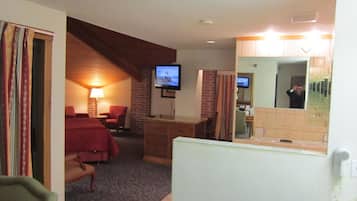 A hotel room with a bed, a desk, a chair, a television, and a bathroom with a mirror.