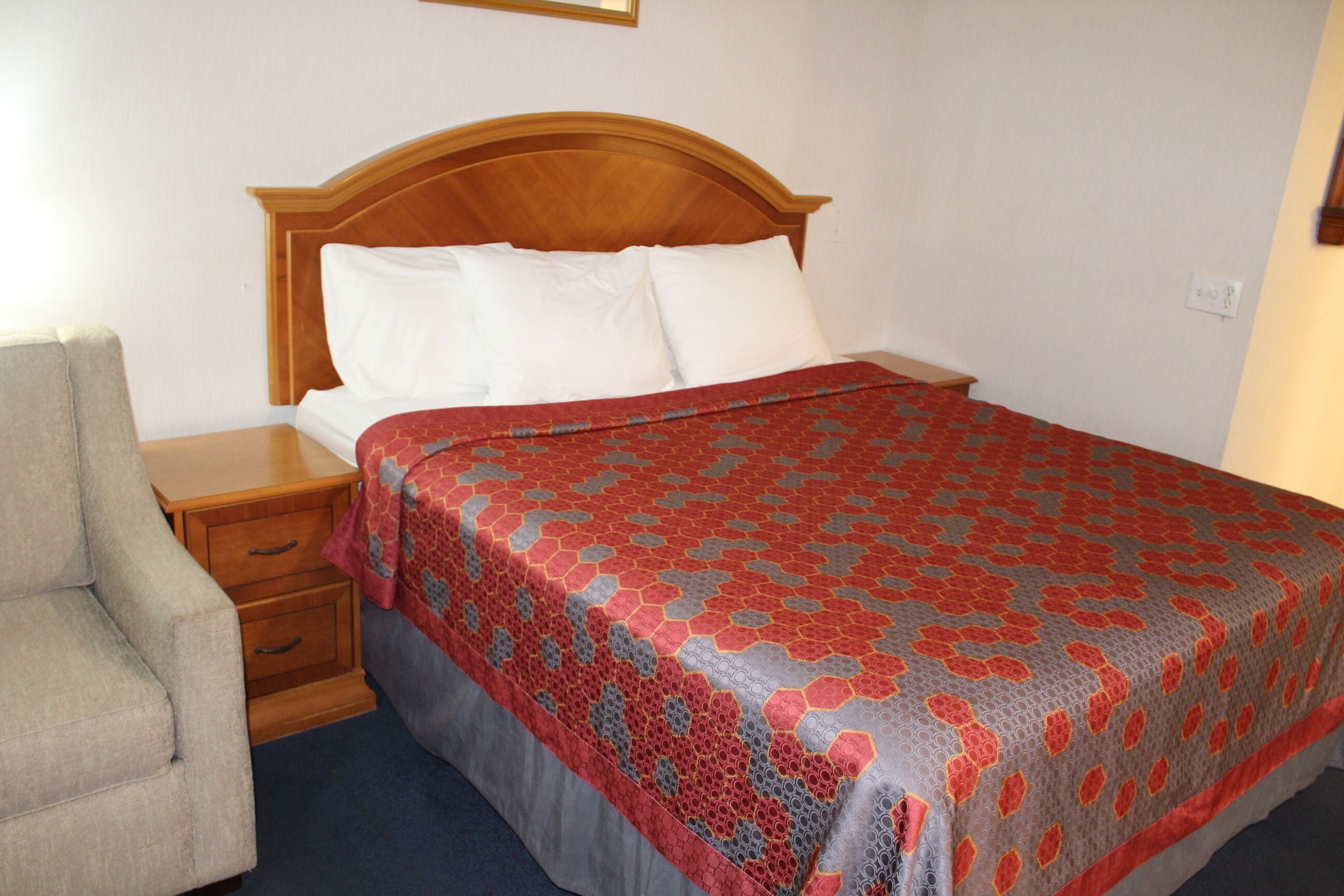 A neatly made bed with a patterned bedspread, a wooden headboard, and a bedside table with drawers.