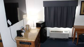 A hotel room with a flat-screen TV, a coffee maker, a microwave, a mini-fridge, a desk, and a window with curtains.