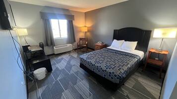A hotel room with a bed, desk, chair, and a small table.