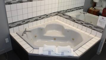 Una bañera independiente grande en un baño de hotel, con un salpicadero de azulejos y un espejo encima.